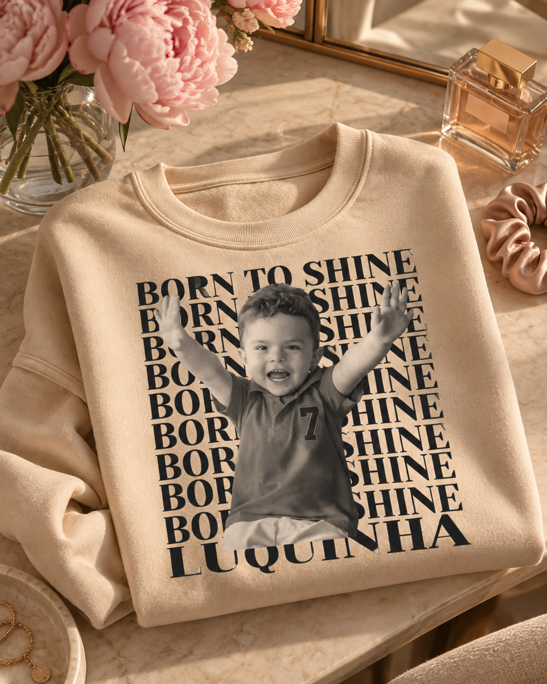 Suéter bege personalizado com foto de bebê Born to Shine dobrado sobre a penteadeira